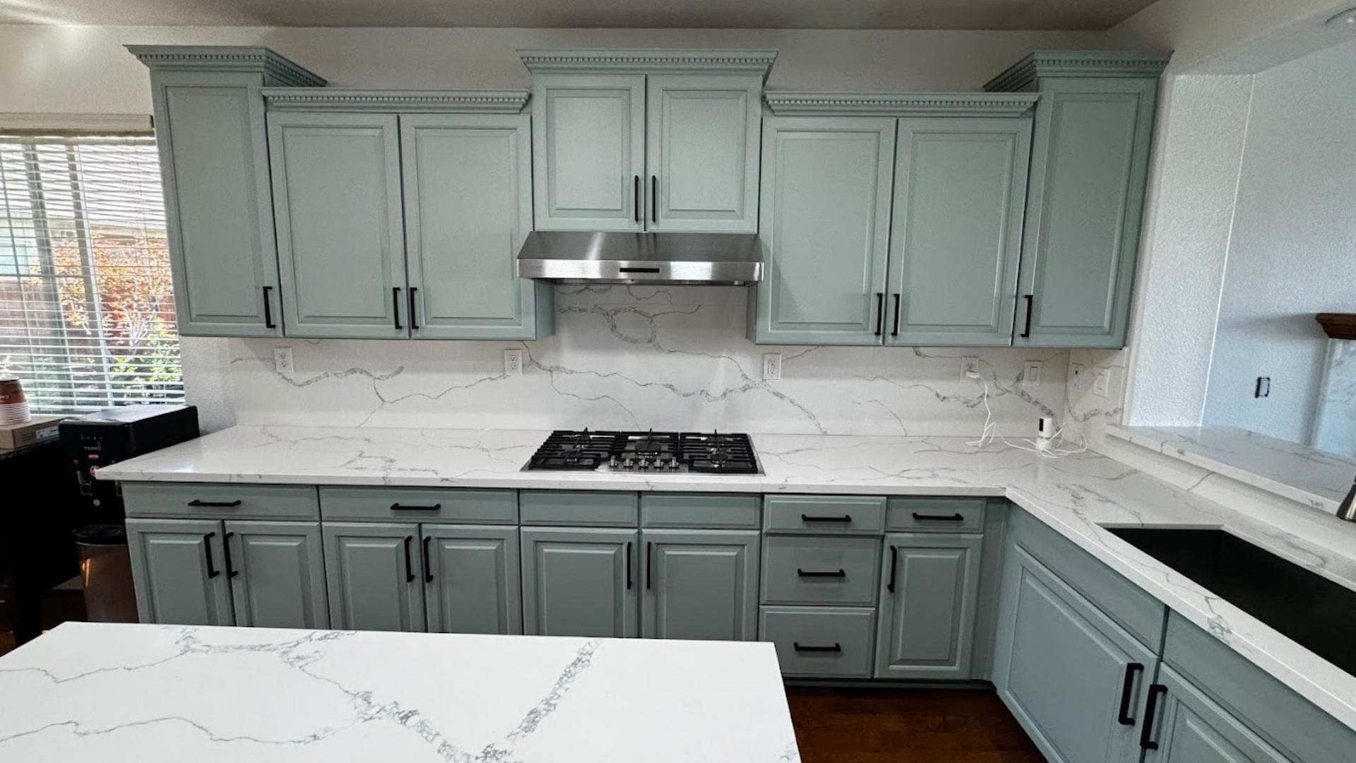 Light green painted kitchen cabinets with dark brown handles in a Pearland Texas kitchen.
