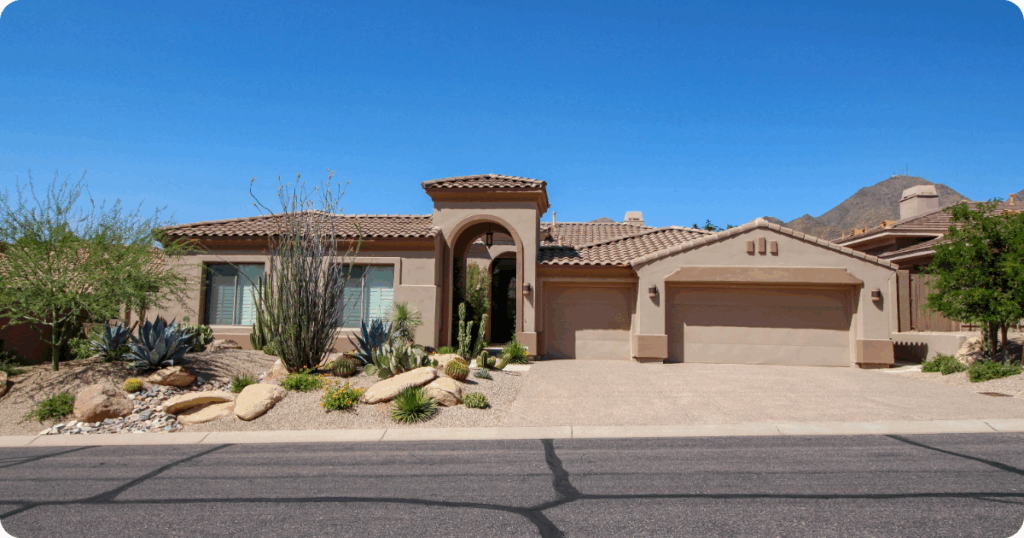 Exterior painting in Phoenix of a Mediterranean-inspired home with smooth stucco walls, tall arched entry, clay tile roof, and a cactus-lined xeriscape front yard by that 1 painter.