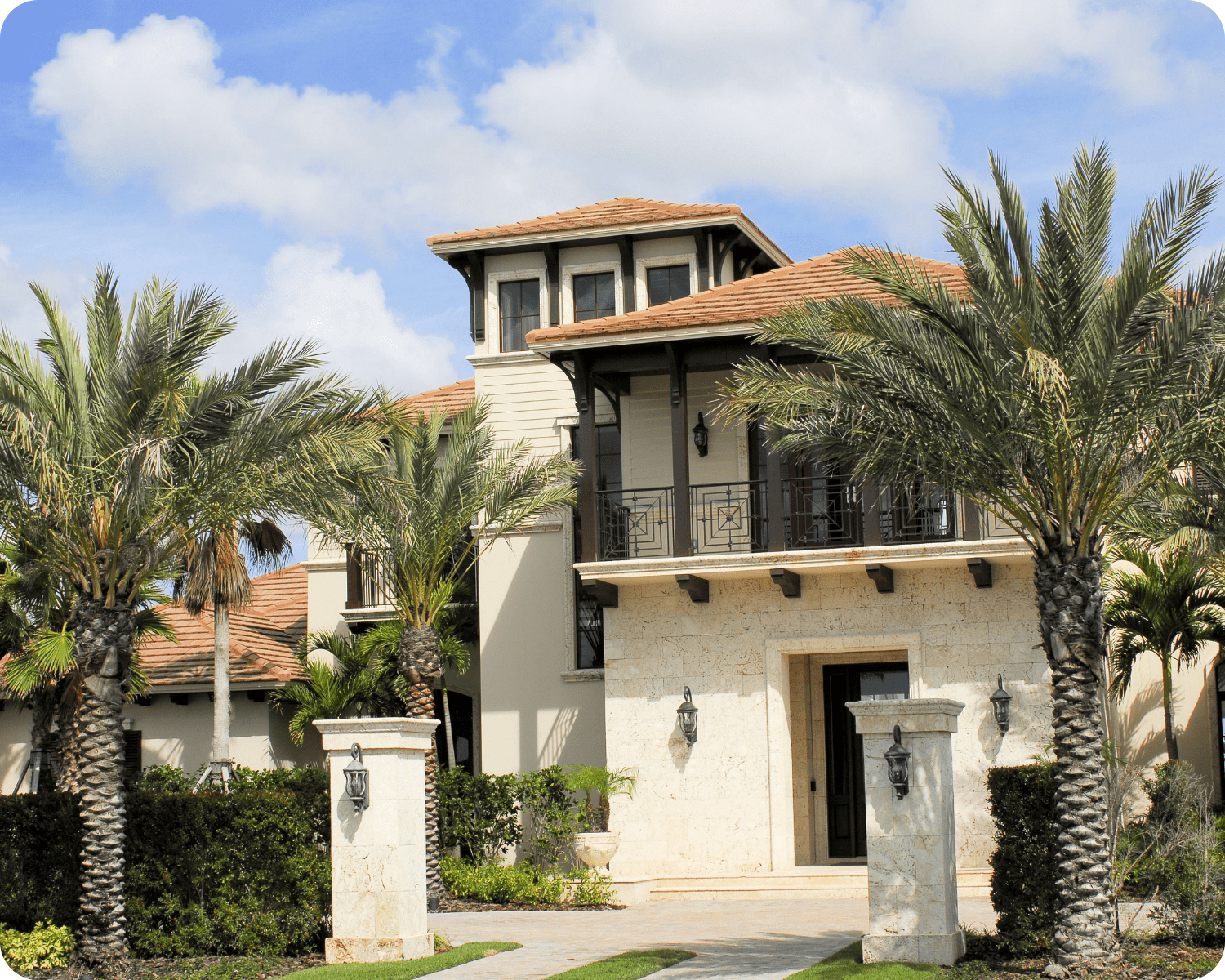 Exterior painting in Sarasota of a luxury coastal villa with limestone exterior, wood trim, upper balcony, and symmetrical palm-lined entrance by that 1 painter.