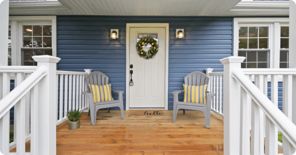 Exterior painting in Scranton of a welcoming front porch with navy blue vinyl siding, white trim, and natural wood decking accented by Adirondack chairs and striped pillows by that 1 painter.
