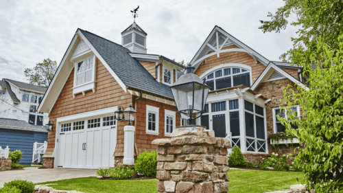 Beautiful tan Cape Cod house with landscaped surroundings having pressure washing completed by professional painters.
