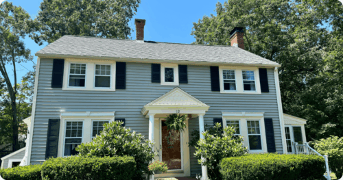 Beautiful gray house with dark window panels, crisp white trim, and a covered white patio painted by professional painters in Merrimack, NH