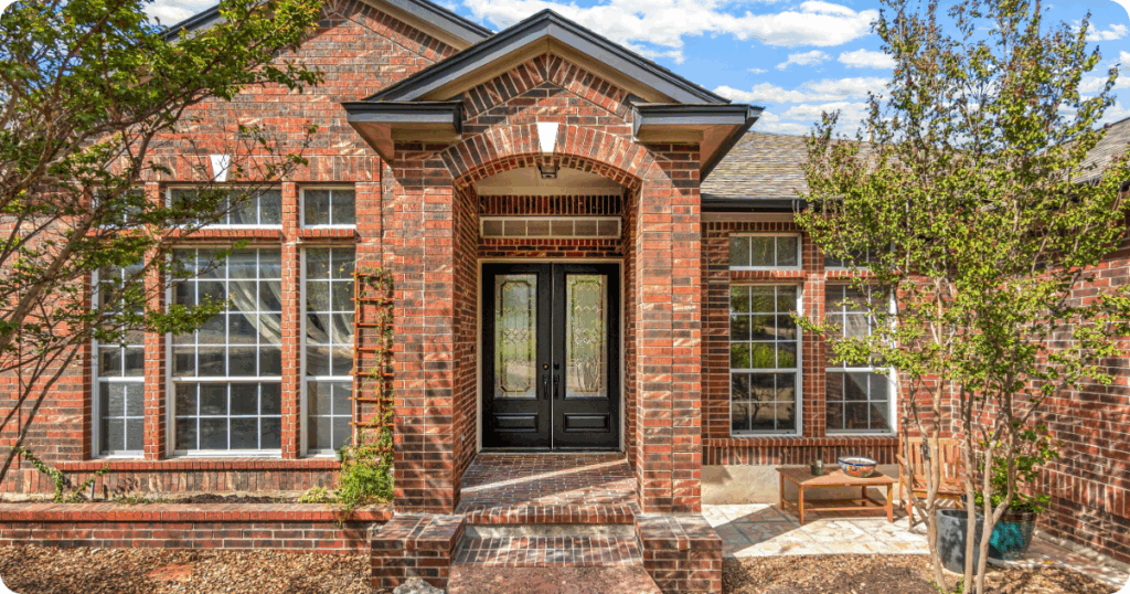 Exterior painting in Treasure Valley featuring a red brick entryway with arched detail, black double front doors with decorative glass, and symmetrical window design by that 1 painter