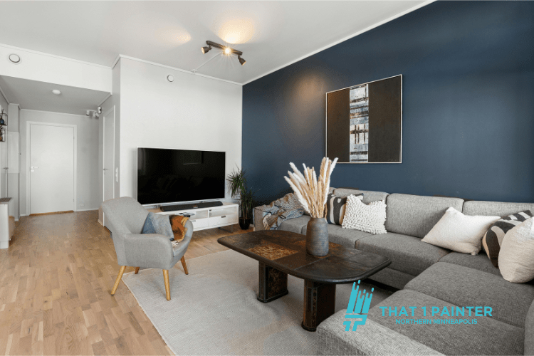 A modern living room featuring a bold navy blue statement wall painted by That 1 Painter Twin Cities. The space showcases a stylish gray sectional sofa, a sleek wooden coffee table, and decorative accents, highlighting the expertise and quality craftsmanship of trusted painting experts in Minneapolis.