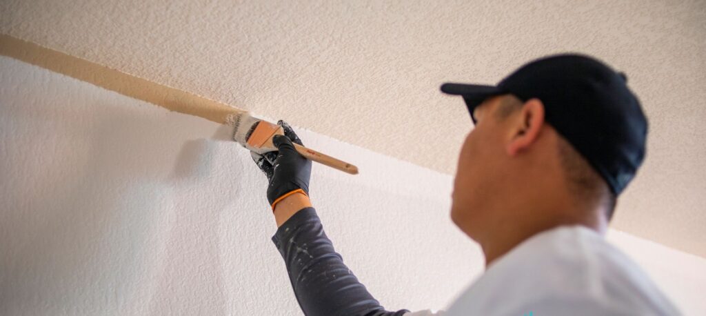 A man using a paintbrush to paint the top of a wall as part of the best house painters in the twin cities interior painting project.