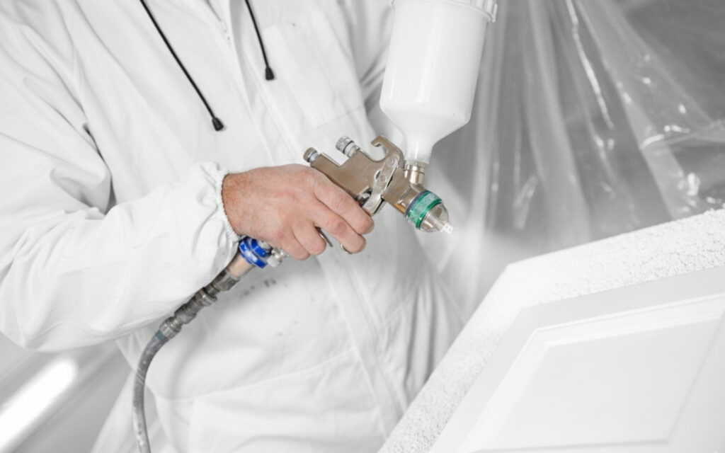 Painting Cabinets Without Removing the Doors? Guide to Better Results 1 Professional painter spraying white paint on a cabinet door to show the painting cabinets without removing the doors is not recommended