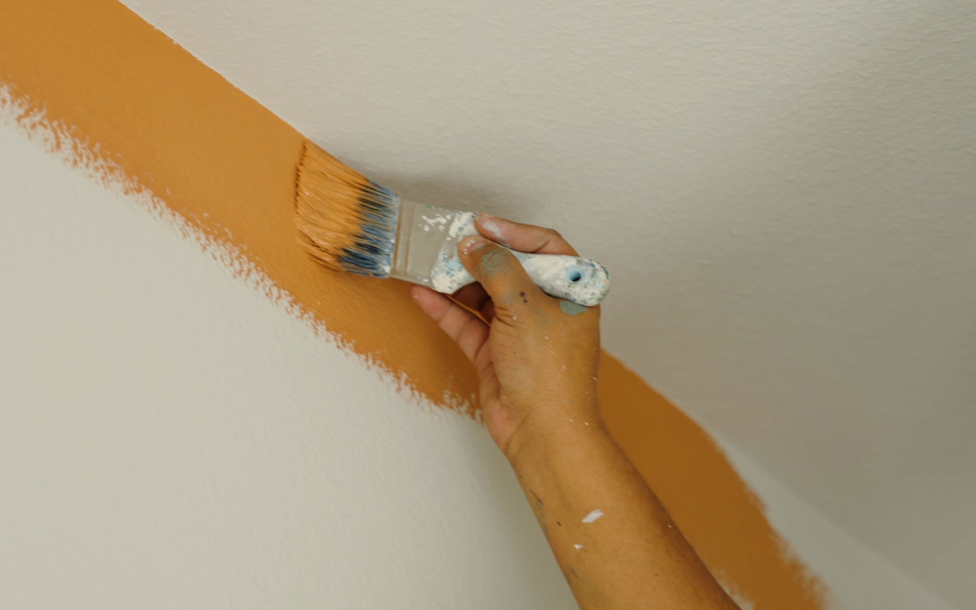 Do You Have to Use Painter’s Tape? The 2026 Guide to Precision Edging and Home Value 1 A hand with a paintbrush cutting in at the top of a wall with yellow paint and no painter's tape