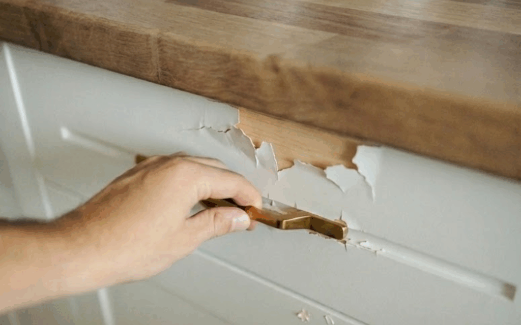 Do I Have to Sand My Cabinets Before Painting? How-To Paint a Beautiful Kitchen 2 A hand holding the handle of a white cabinet drawer that has peeling cabinet paint due to not sanding