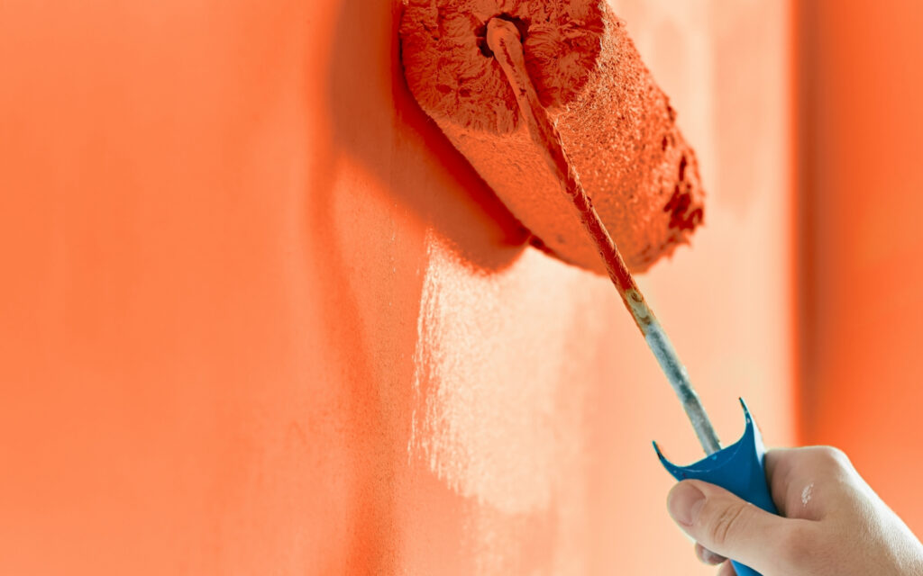 Water-Based vs Oil-Based Paint - How-to Choose the Best Paint 2 a close up of a hand holding a paint roller using orange water-based paint on a wall